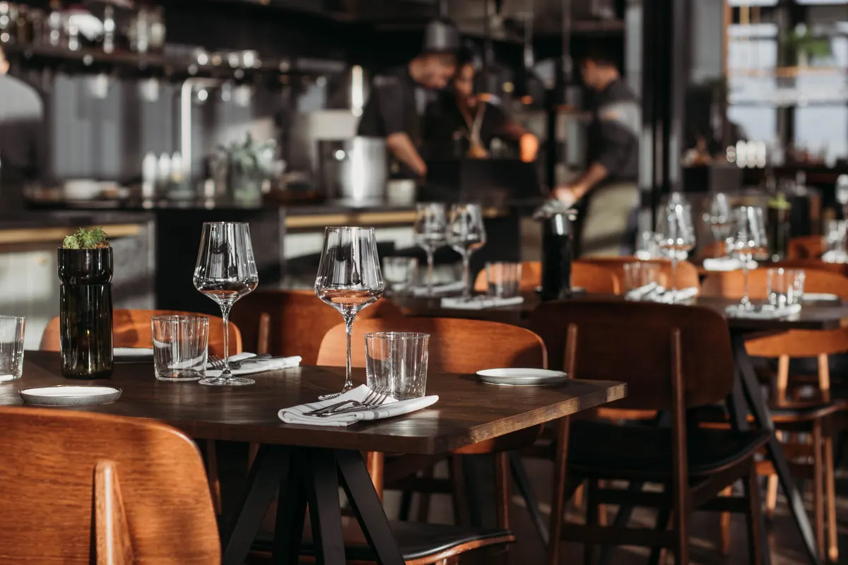 Set restaurant tables with wine glasses in front of an open kitchen