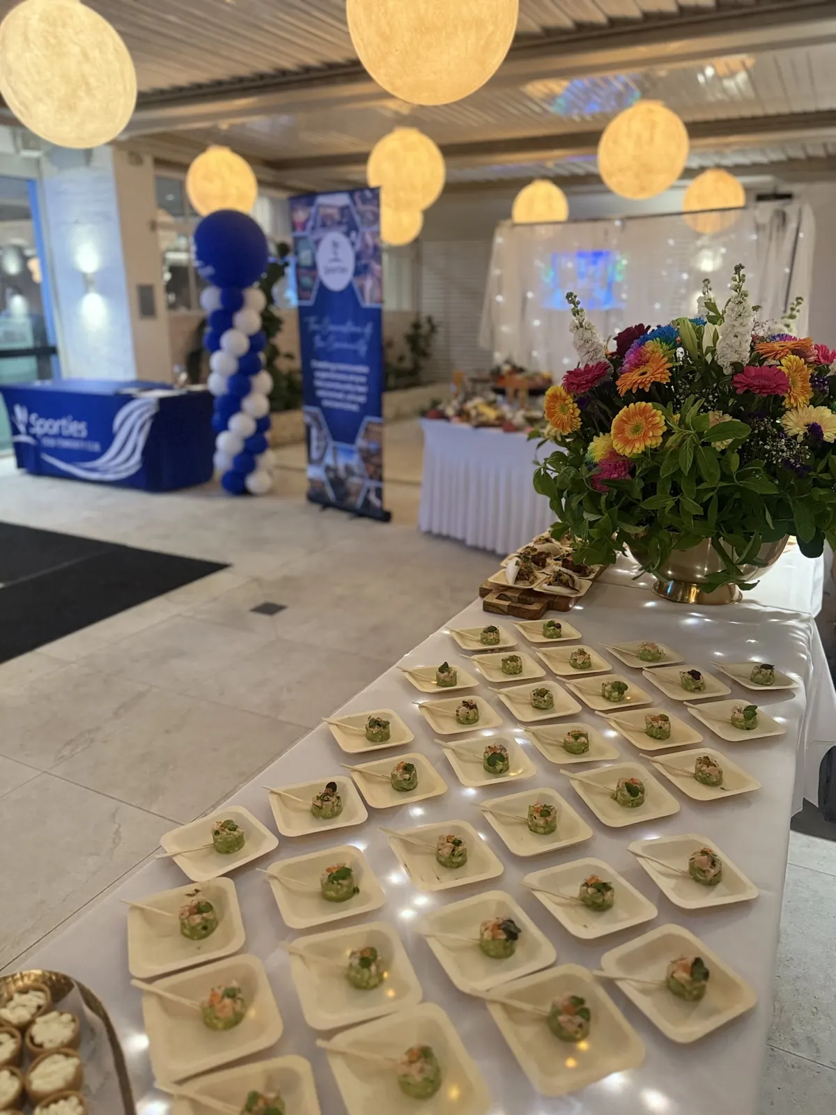 Canapés laid out at a function with flowers and a blue balloon arch