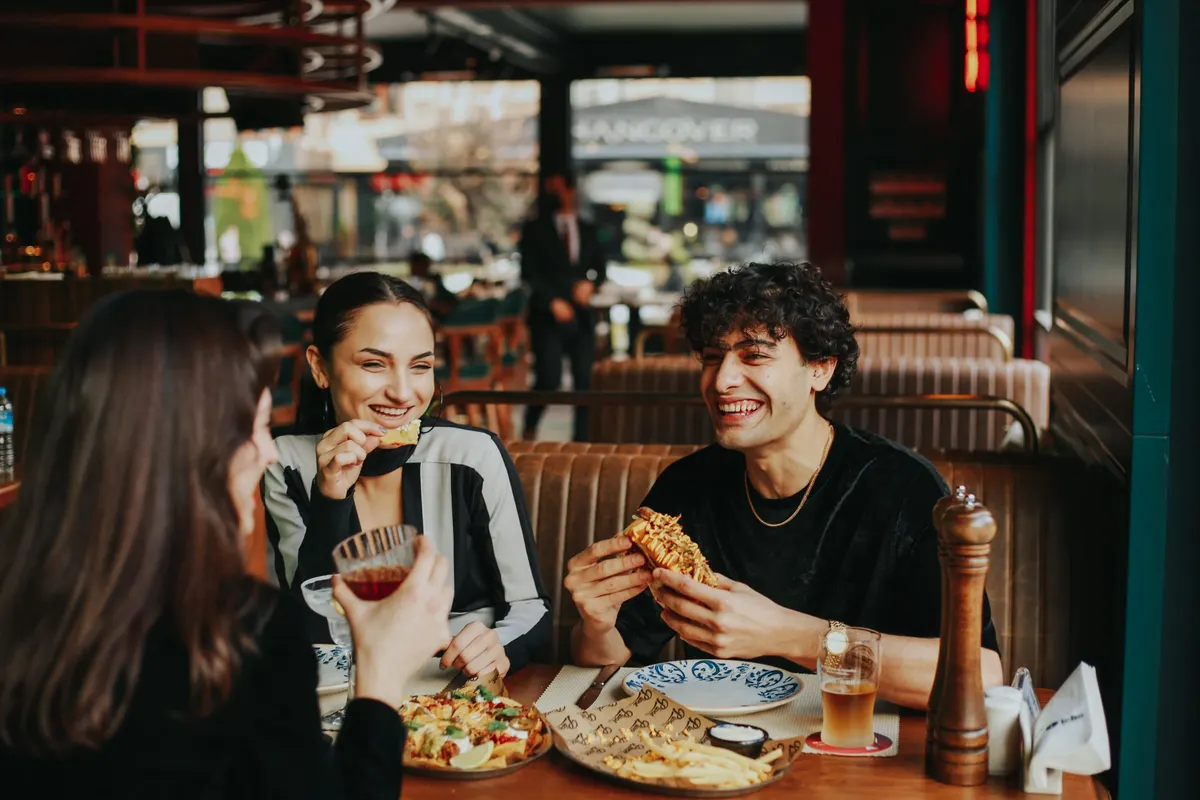 Friends laughing over a shared meal in a warm brasserie booth