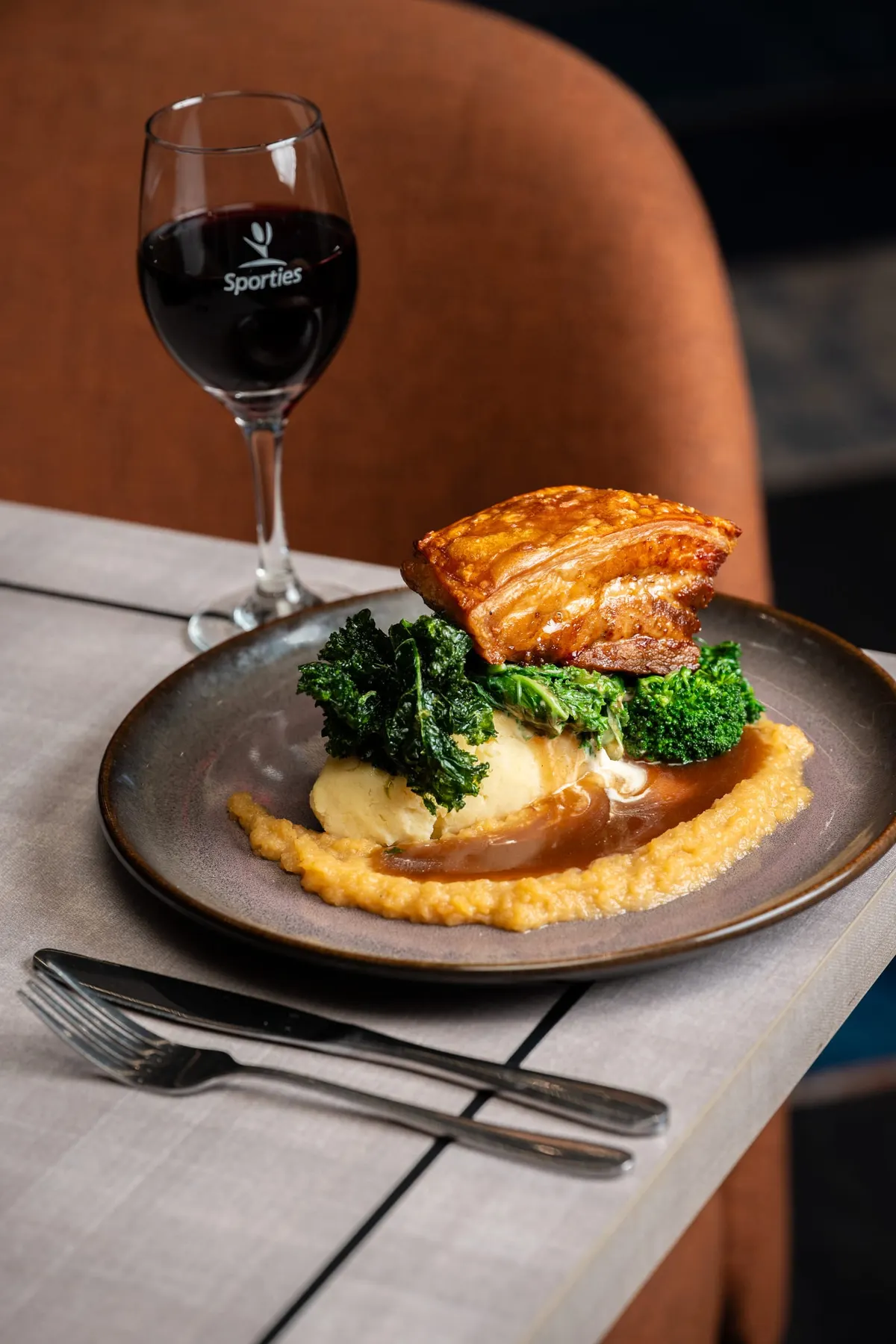 Crispy pork belly with pumpkin purée and greens, red wine alongside