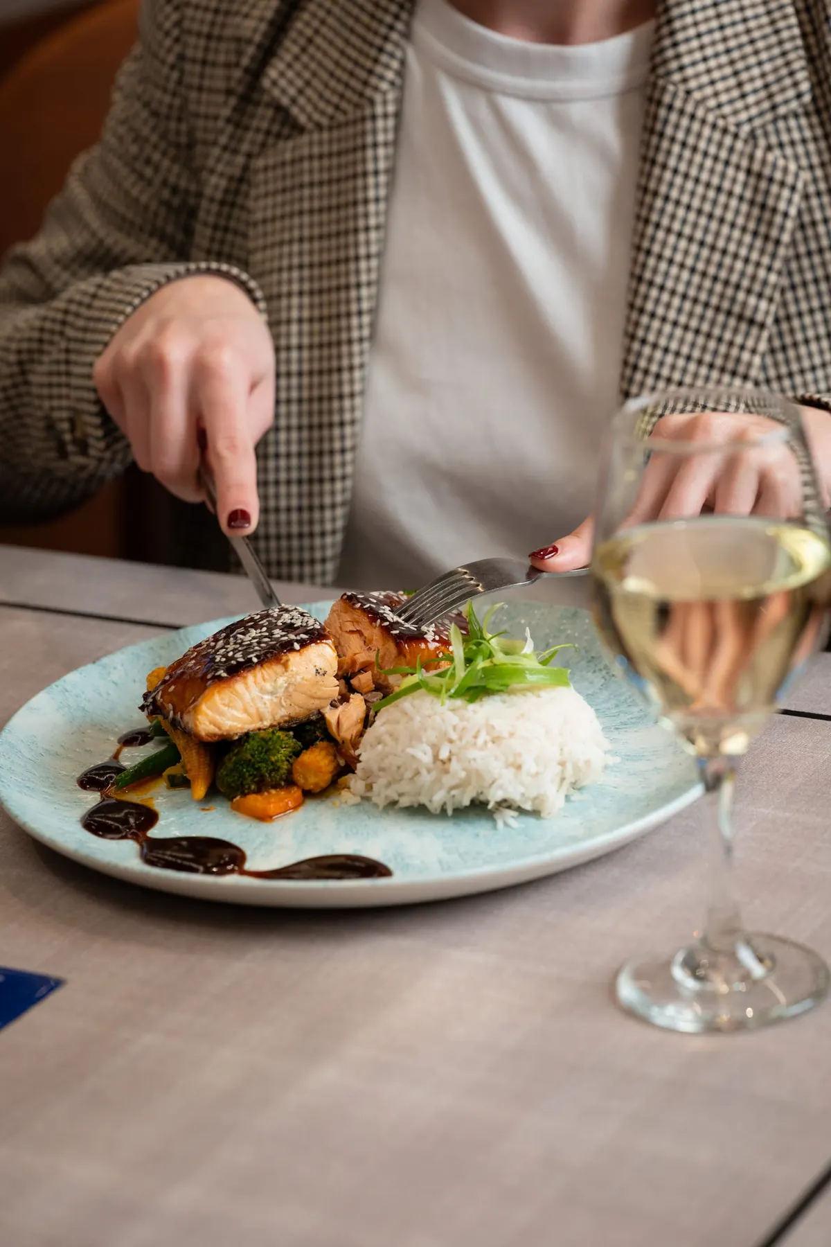 Guest cutting into glazed fish with rice and a glass of white wine