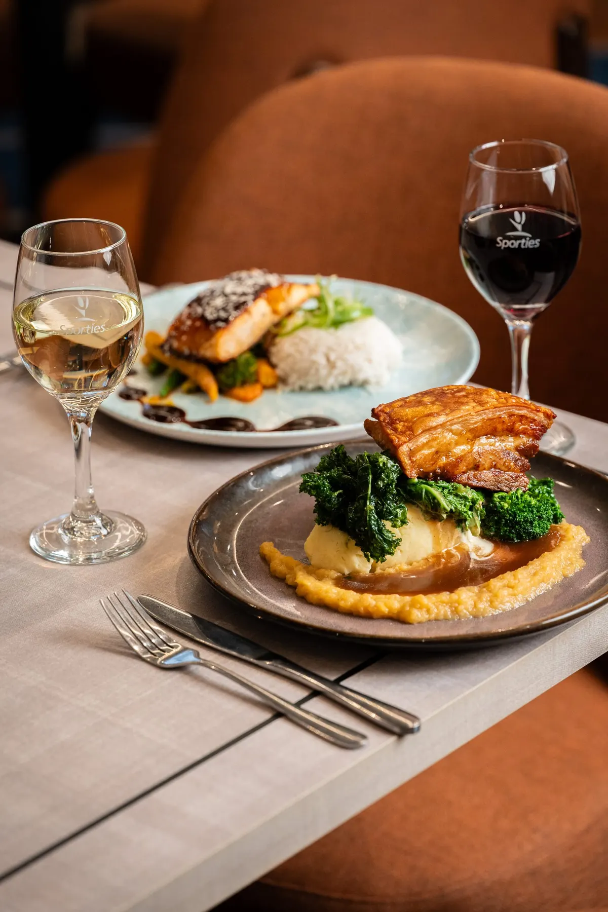Pork belly and glazed fish served side by side with red and white wine